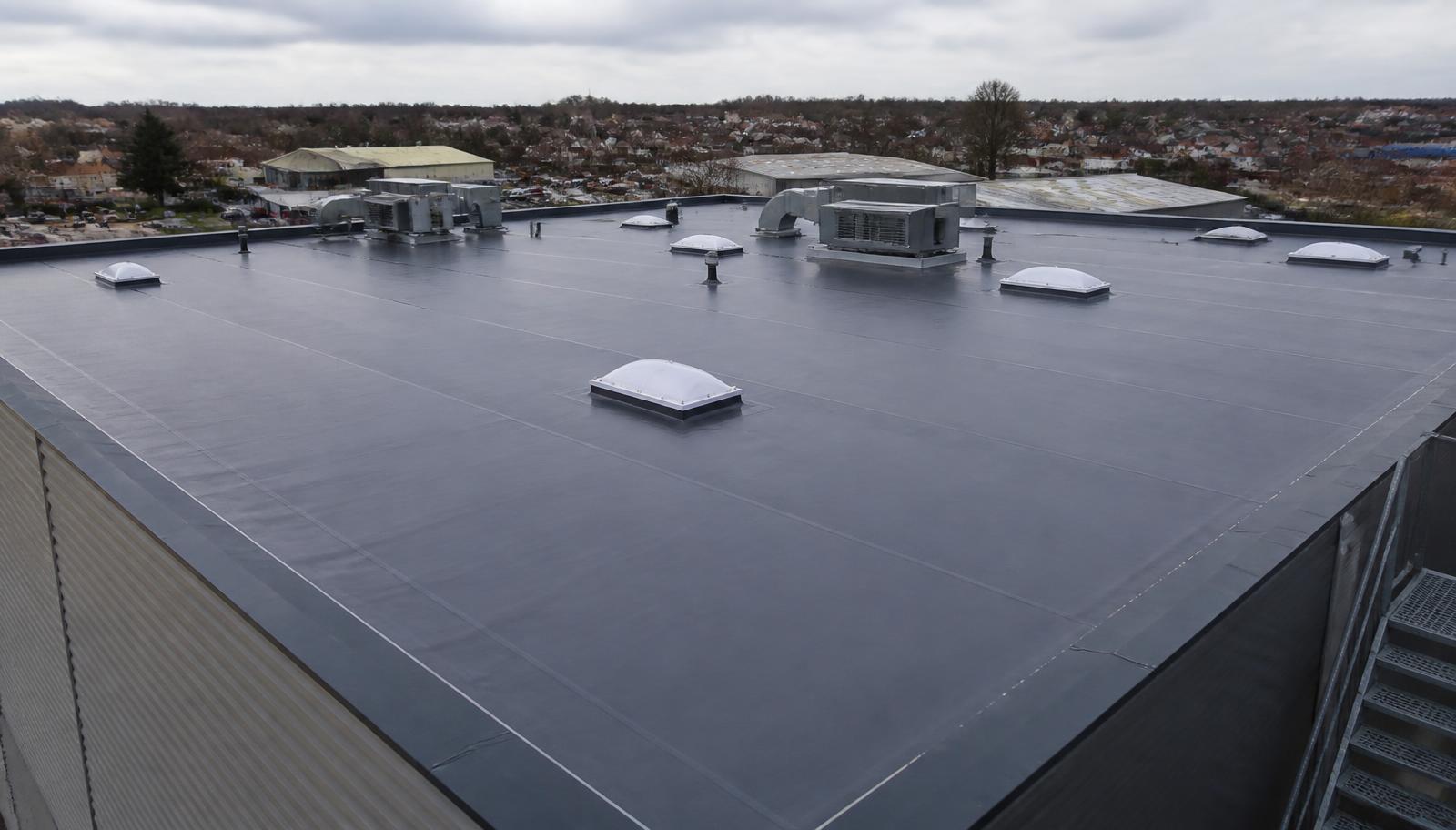 Aerial view of a large newly installed dark grey single-ply commercial flat roof on a UK industrial unit with roof lights, plant units and parapet edge trims